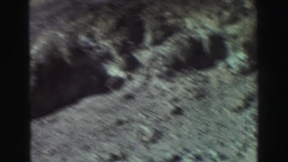 1969 Lake Tahoe 8mm frame showing pale dirt, scattered rocks, and shallow dark hollows in a dry landscape.