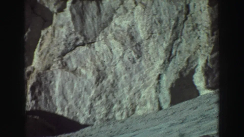 1969 Lake Tahoe 8mm frame showing a rough rock wall, sloped dirt foreground, and dark shadow at the base.