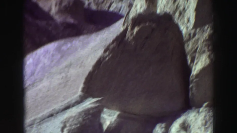 Lake Tahoe rock formations recorded on 8mm film, with rounded stone surfaces, deep shadows, and a purple-blue tint.