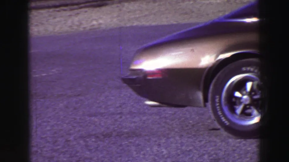 1969 Lake Tahoe frame showing the front section of a bronze-toned classic car, wheel, hood, and rocky roadside background.