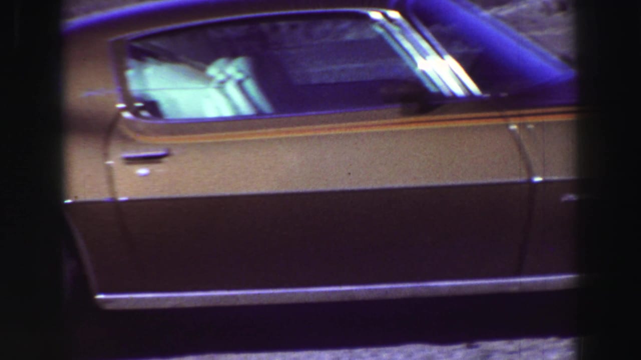 Side view of a gold and dark sports car partly framed by black film edges.