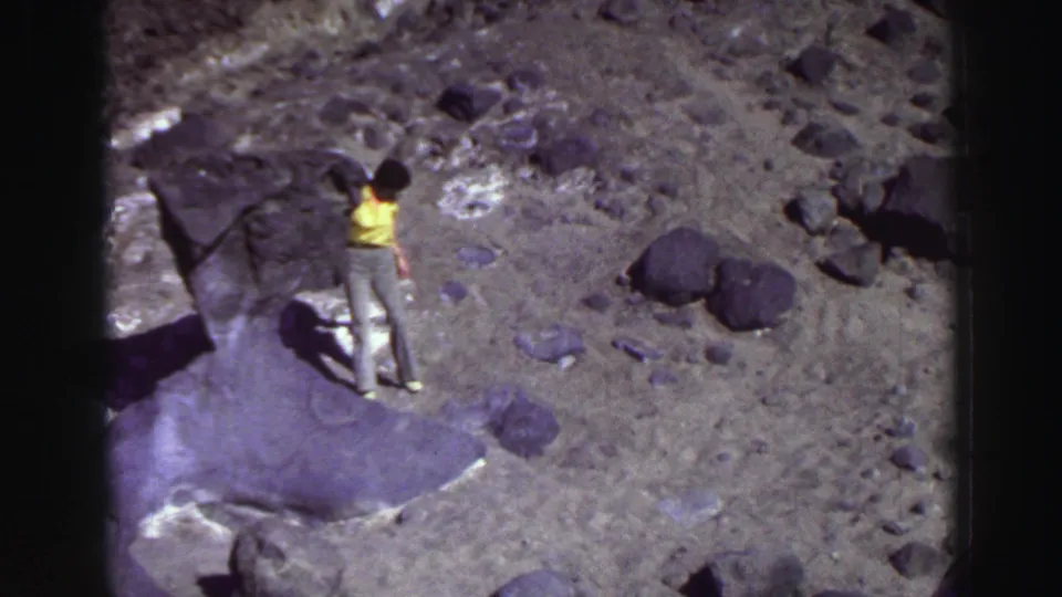A second person in a yellow shirt stands on rocky Lake Tahoe terrain near dark boulders in this 1969 8mm home-movie frame.