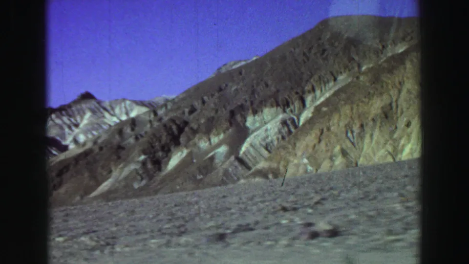 1969 8mm landscape frame with a dark ridge, pale exposed rock bands, and an empty foreground in the listed California setting.