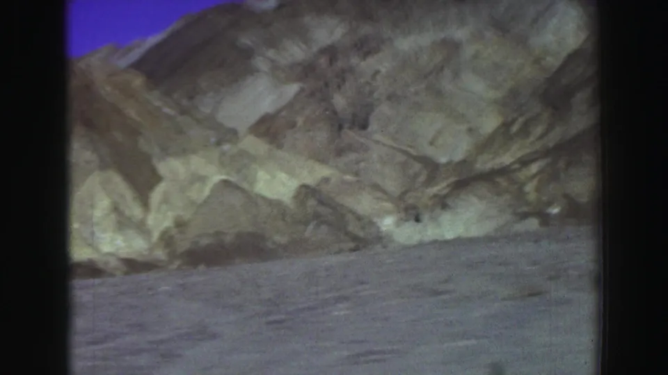 Soft 8mm frame of eroded pale and brown mountain slopes with barren ground below, consistent with the listed 1969 California landscape clip.