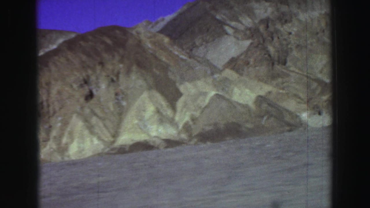 Desert road view with pale eroded hills and a purple-blue sky.