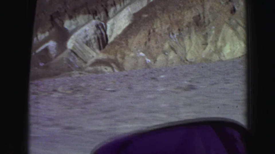 1969 home-movie travel footage shows eroded desert hills and pale roadside terrain, with part of the vehicle interior visible along the lower frame.