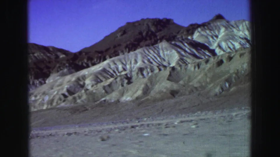 A supported Lake Tahoe-area 1969 8mm frame shows open desert terrain, striated pale mountains, a darker ridge, and a deep blue-purple sky.