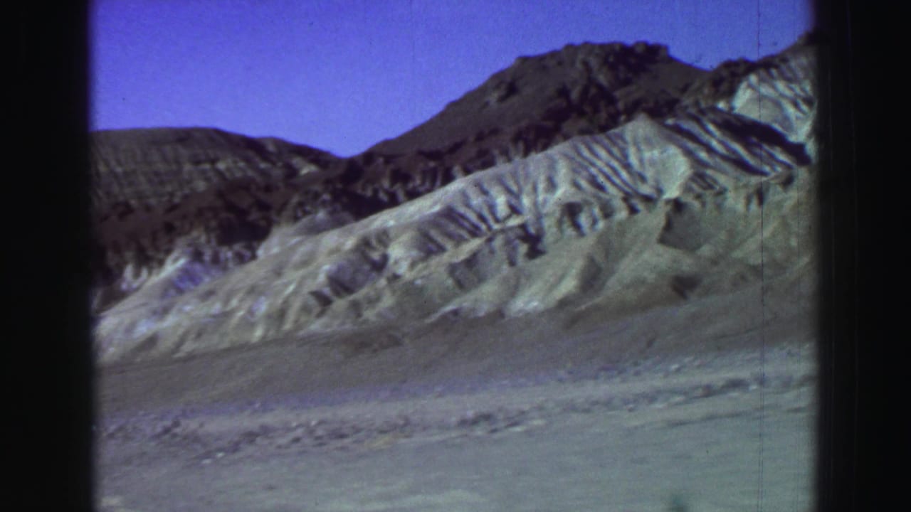 Eroded mountain slopes under a blue-purple sky with 8mm frame borders.