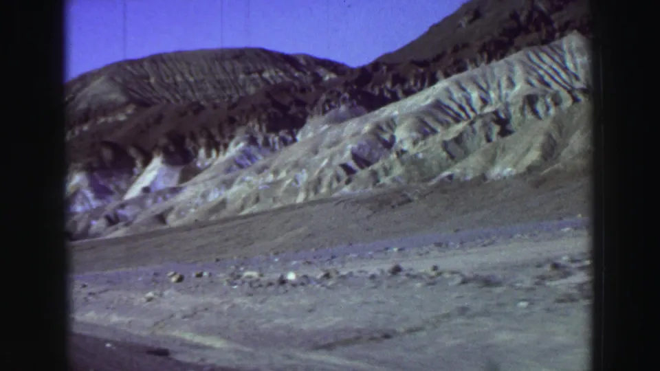 Archival 8mm view of rugged Lake Tahoe-area terrain, with pale eroded slopes, rocks, and dark hills beyond.