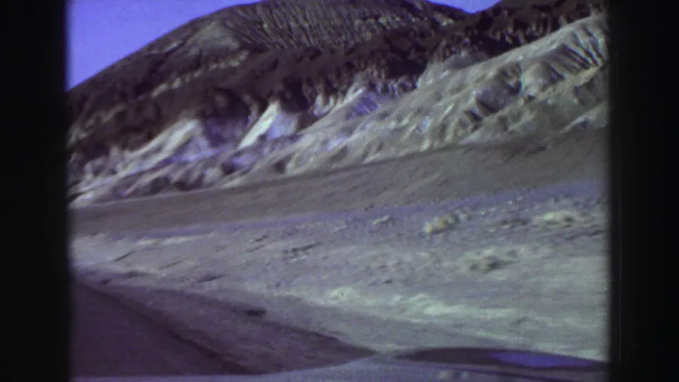 1969 8mm frame looking along a mountain road edge toward eroded Lake Tahoe-area slopes and open terrain.