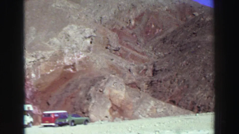 1969 Lake Tahoe-area roadside stop with a white camper van, red station wagon, and green sedan below reddish rocky hills.