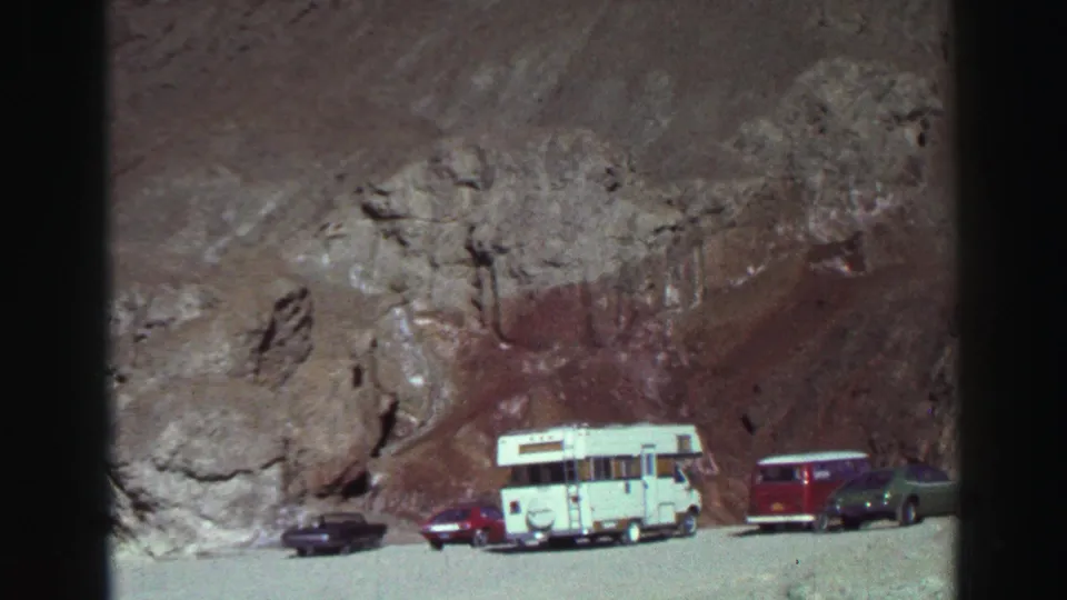 1969 Lake Tahoe roadside view with a dark car, red car, white camper, red wagon, and green car beneath a rocky mountain face.