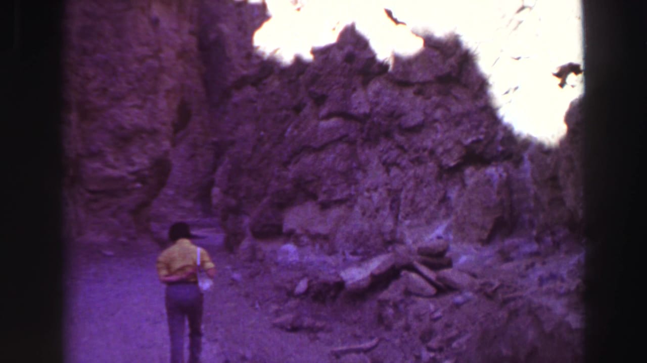 Person in a yellow shirt walking into a narrow rocky canyon under strong sunlight.