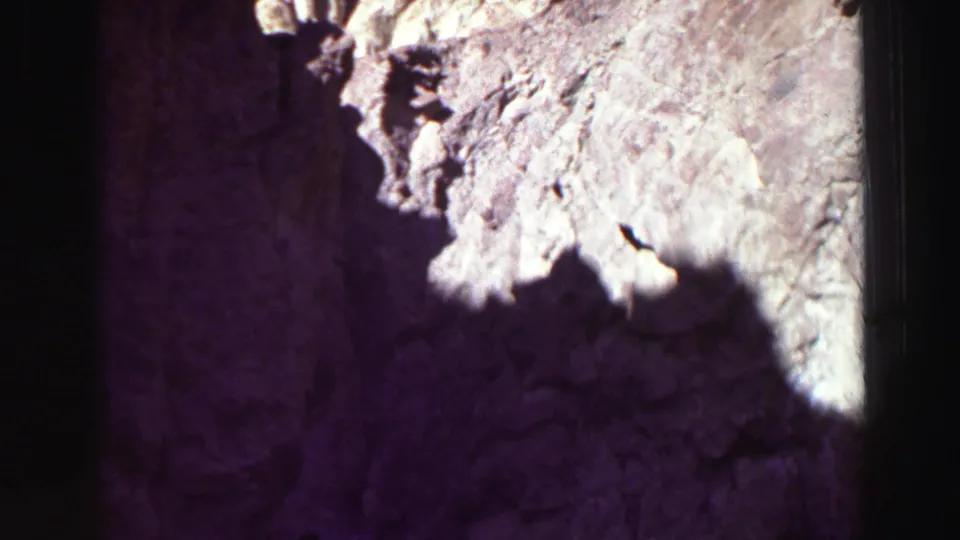 8mm frame of a rugged canyon wall near Lake Tahoe, with strong sunlight, dark shadow, and purple color shift from the film scan.