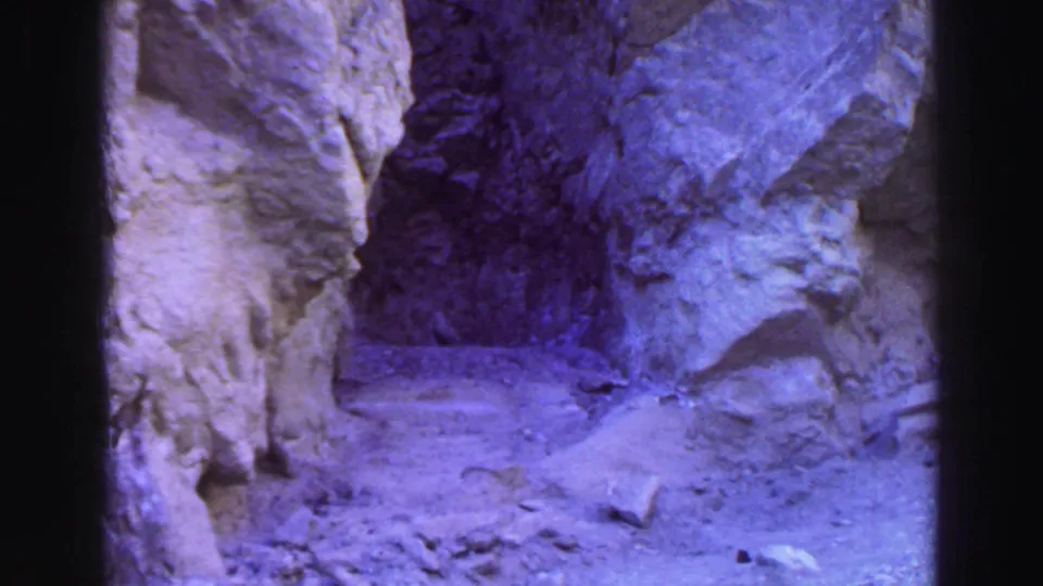 Shadowed canyon passage near Lake Tahoe on 8mm film, showing rough rock walls, scattered stones, and a narrow dusty path.