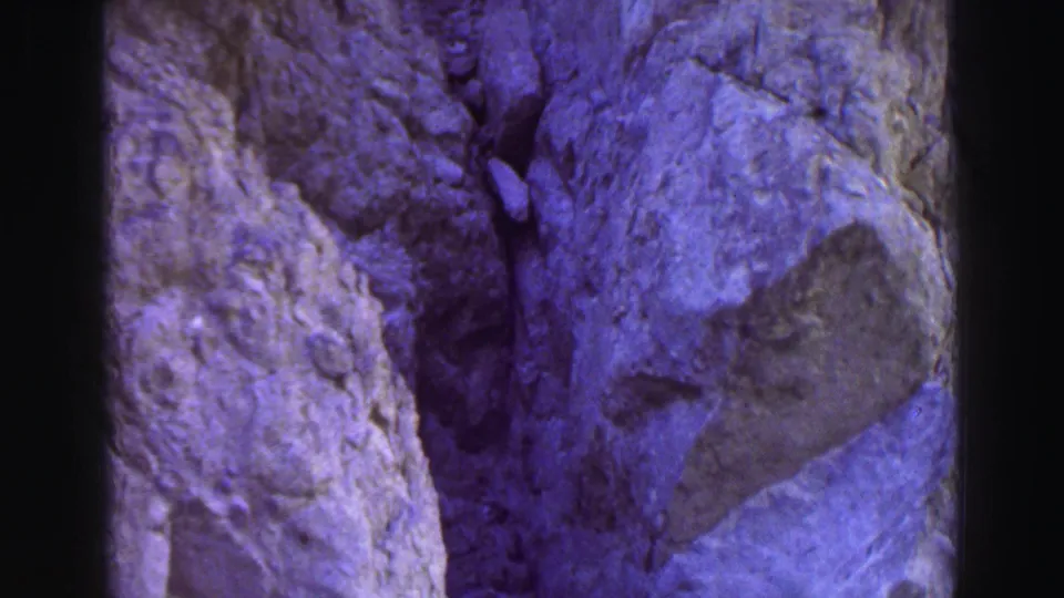 1969 Lake Tahoe home-movie still showing uneven rocky ground, large stone faces, and loose fragments along a mountain trail.