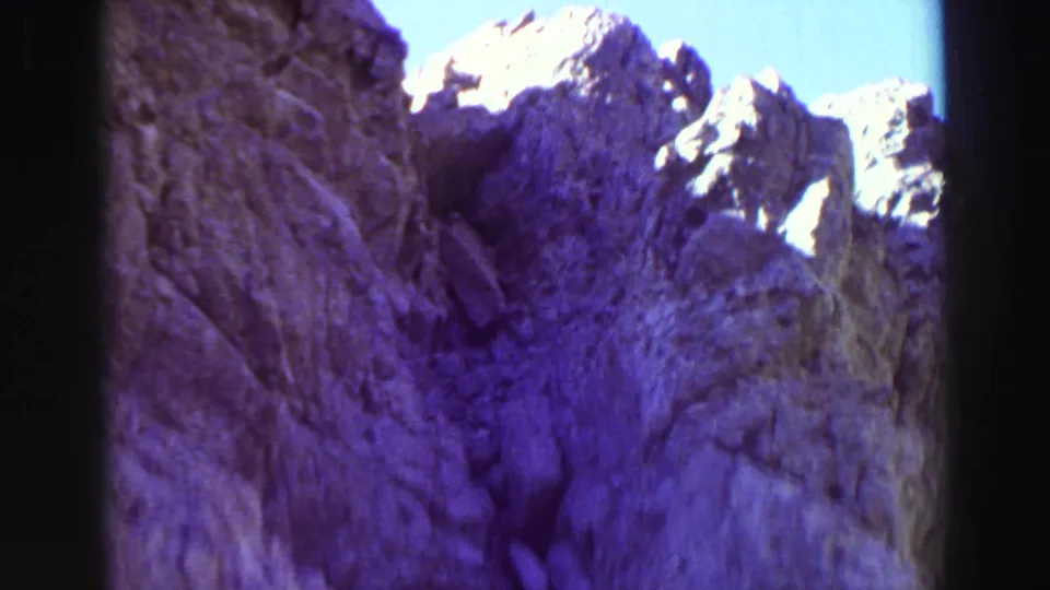 1969 Lake Tahoe 8mm frame showing a steep shadowed rock face with jagged bright peaks against a clear blue sky.
