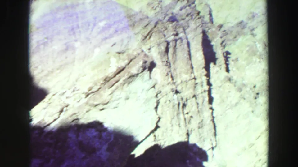 1969 8mm Lake Tahoe close-up of pale layered stone, visible cracks, dark shadows, and rounded black film-frame corners.