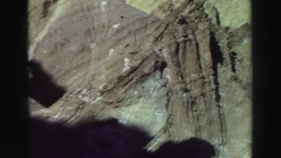 1969 8mm Lake Tahoe footage showing a sloped rock surface with vertical cracks, muted film color, grain, and a broad shadow below.