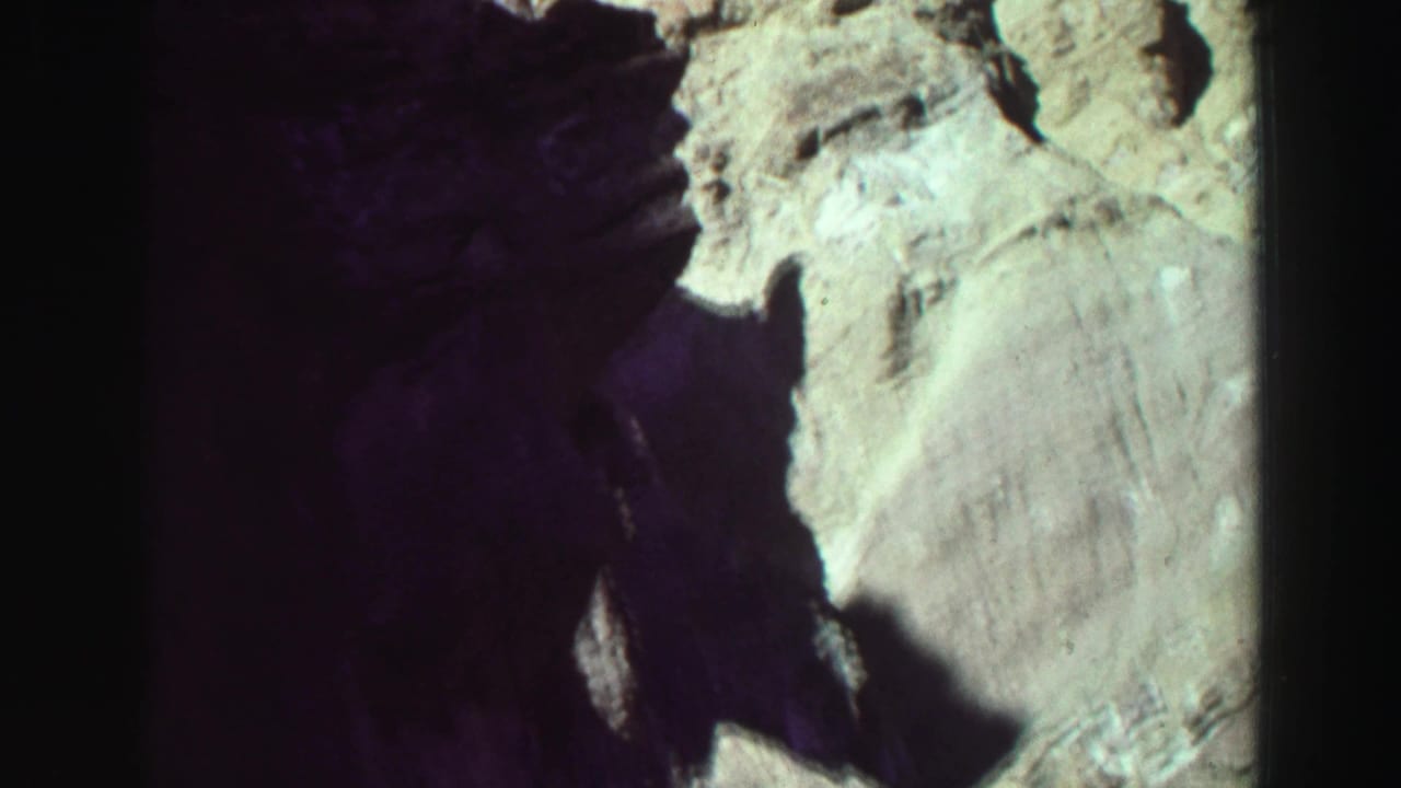 Shadowed rocky canyon wall with pale sunlit stone and dark film borders.