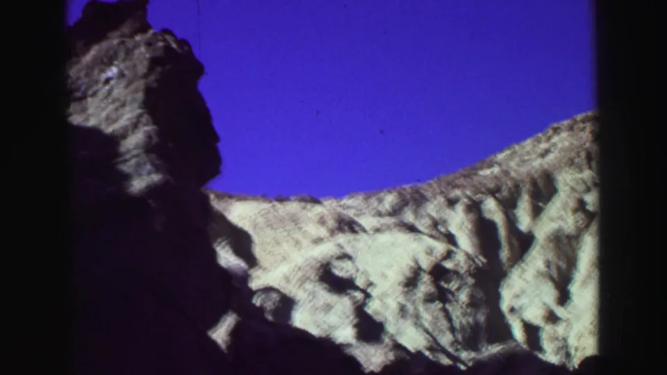 1969 8mm Lake Tahoe frame showing a dark vertical cliff silhouette beside pale canyon rock and open blue sky.