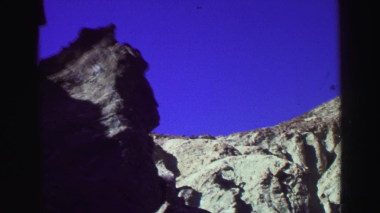Rocky mountain outcrop and pale ridge under a saturated blue sky.