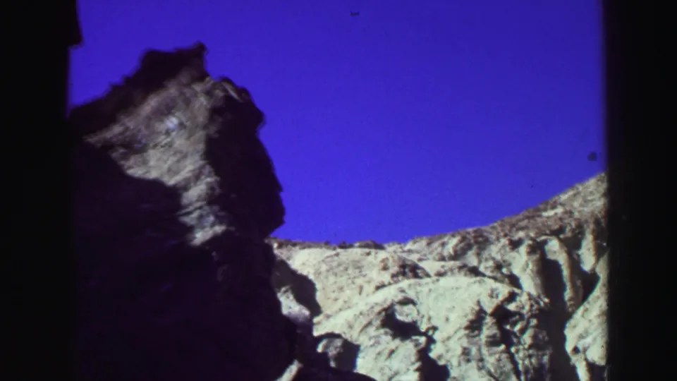 1969 Lake Tahoe home-movie frame showing a rugged rock outcrop, sunlit ridge, and deep blue sky with visible 8mm frame edges.