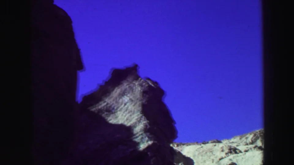 1969 Lake Tahoe landscape frame with a dark foreground rock mass, smaller jagged outcrop, pale ridge, and blue sky.
