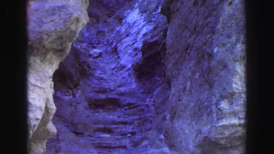 1969 Lake Tahoe 8mm frame showing steep gray rock walls with blue-purple color shift inside a narrow rocky passage.