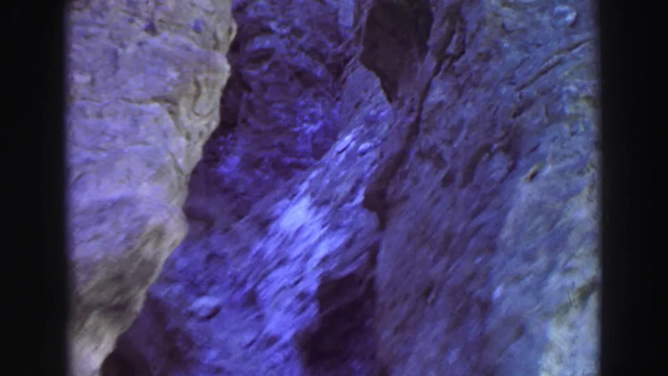 1969 Lake Tahoe 8mm frame showing a rugged vertical rock face with shadowed cracks and strong blue-purple film color.