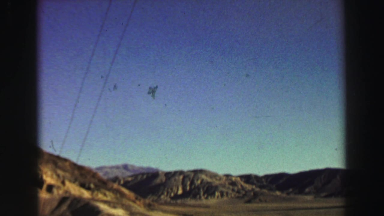 Arid hills and distant mountains under a blue sky, seen through dark 8mm frame edges.