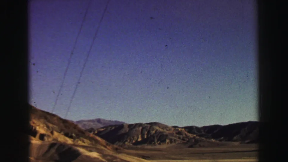 1969 Lake Tahoe-area driving view with rugged hills, distant mountains, utility lines, and visible 8mm gate edges.