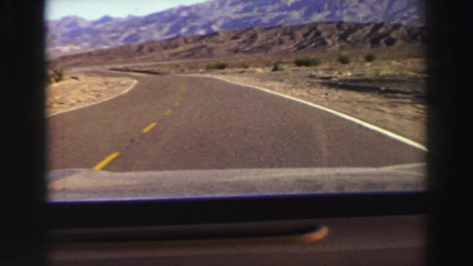 End frame of the 1969 8mm road view, with the highway bending through arid terrain toward distant mountains.