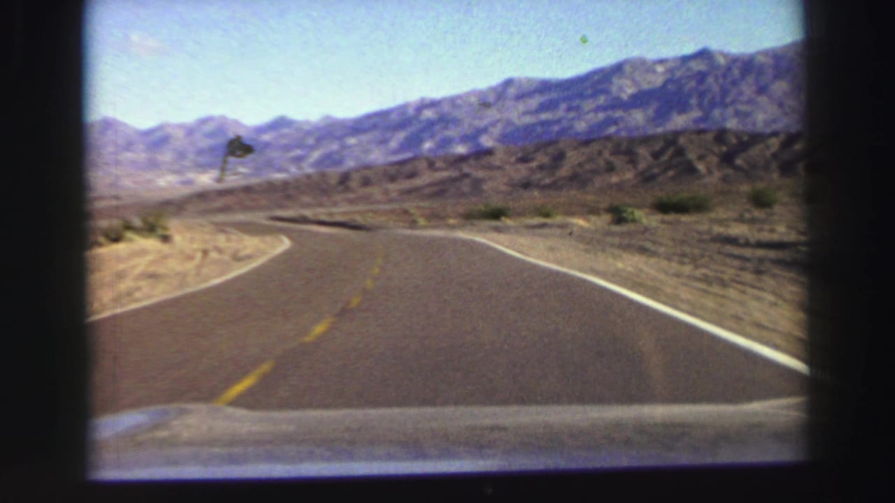 Two-lane desert road curving toward distant mountains under blue sky.