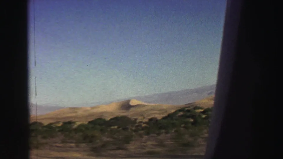 1969 home-movie frame from the Lake Tahoe area showing roadside scrub, tan hills, and distant mountains through a vehicle window.