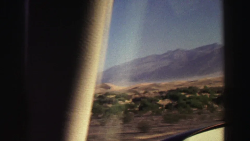 Moving 8mm view near Lake Tahoe with motion blur, window edge, dry hills, scattered shrubs, and a distant mountain ridge.
