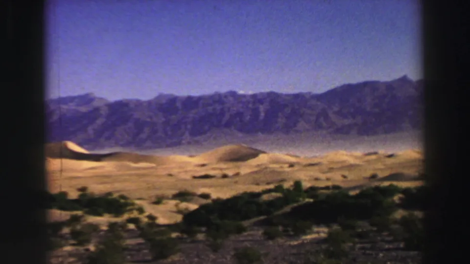 1969 8mm home-movie frame showing golden dunes, sparse shrubs, and a distant mountain range in the Lake Tahoe metadata location.