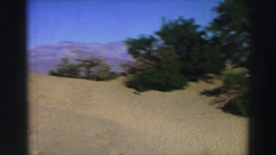 Lake Tahoe-area 1969 home-movie frame showing sandy terrain, scattered shrubs, and distant mountain ridges.
