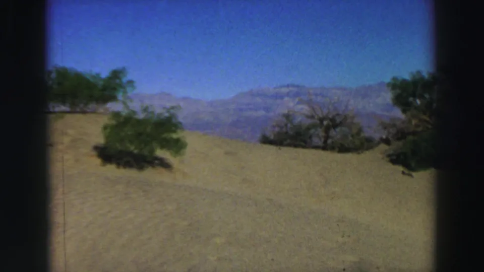Late-1960s Lake Tahoe-area home-movie view of sandy terrain, sparse bushes, and blue mountains in the background.