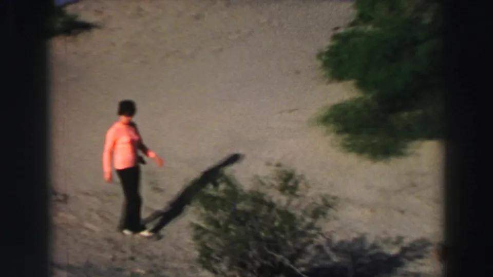 The woman continues across sandy ground near low vegetation, filmed from a high handheld angle at Lake Tahoe.