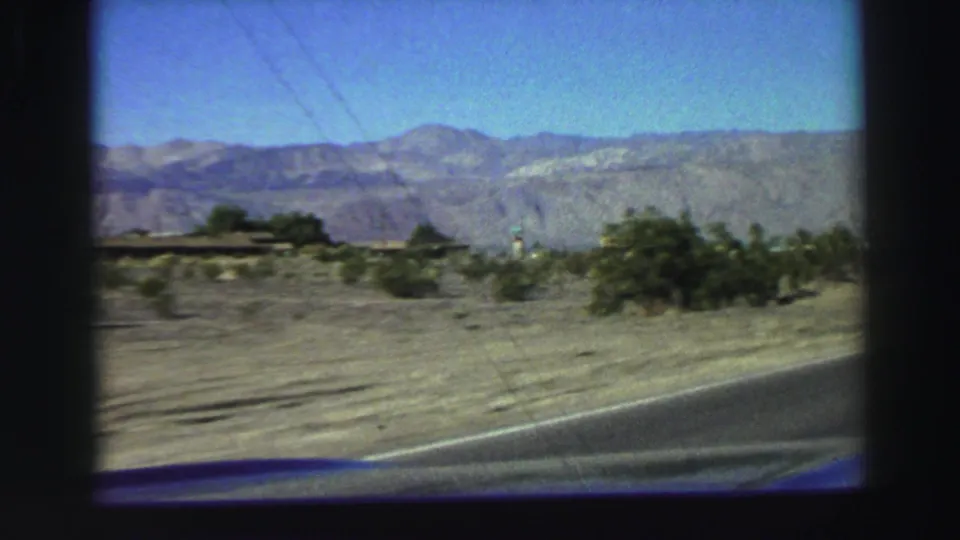 Moving 8mm road view near Lake Tahoe with scrubland, pavement, distant mountains, and clear blue sky.