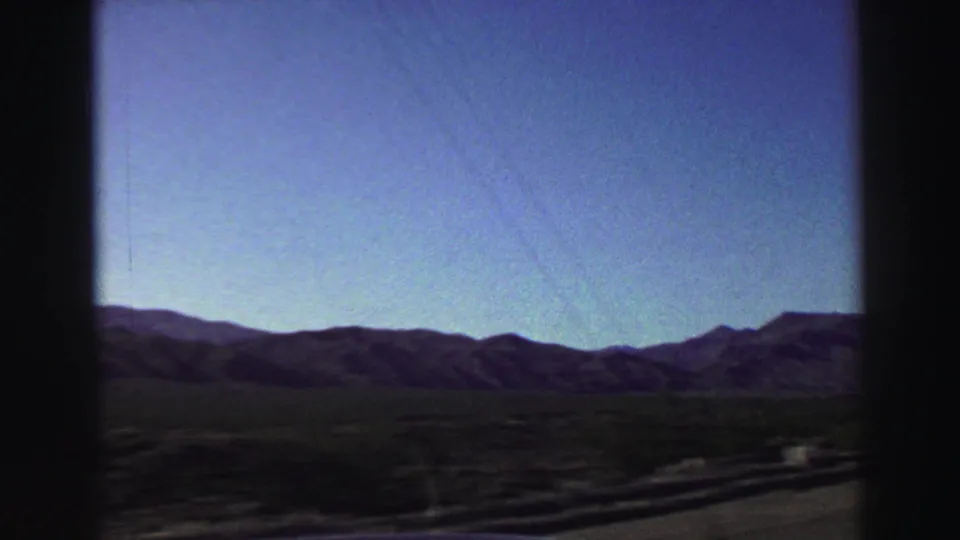 Moving-vehicle view near Lake Tahoe in 1969, looking across a dark foreground toward low mountain ridges under a clear blue sky.