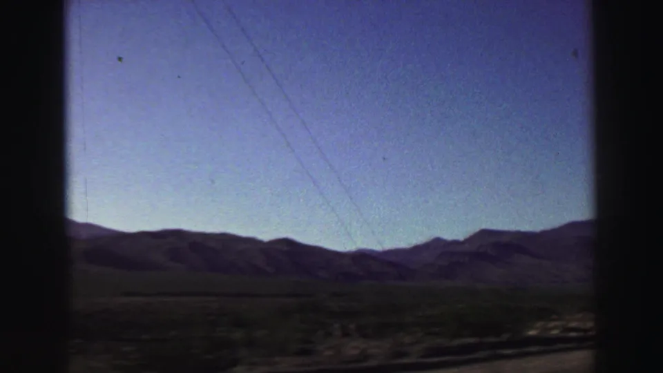 1969 home-movie frame showing distant mountains, utility lines crossing the sky, and open terrain viewed from a moving car near Lake Tahoe.