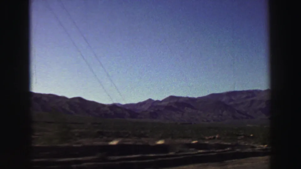 Late-1960s Lake Tahoe-area travel footage with a mountain range, utility lines, open roadside ground, and slight motion blur from the moving vehicle.