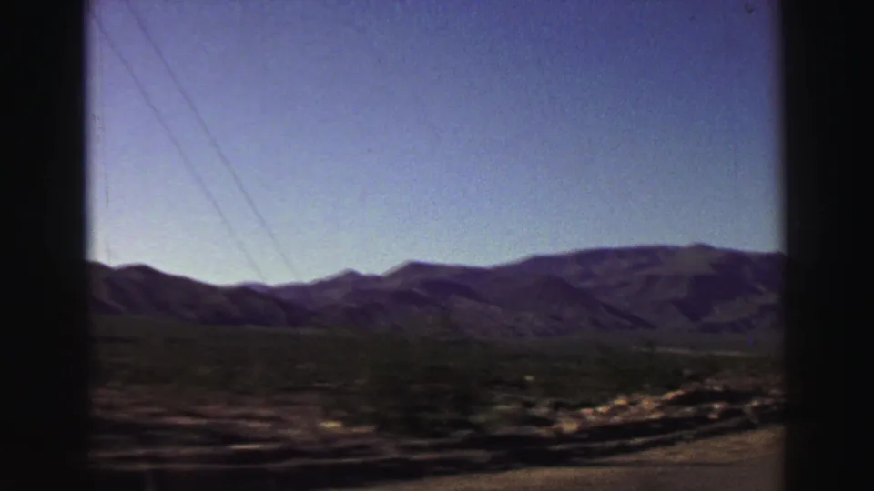 1969 Lake Tahoe region home-movie frame showing mountain ridges, blue sky, and roadside desert terrain from inside a moving car.