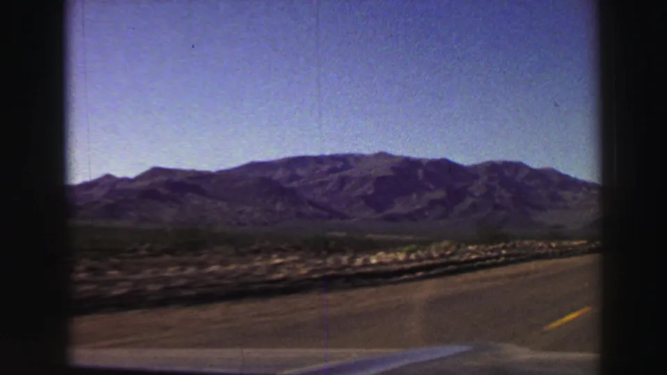 Lake Tahoe region road view from inside a car, with a highway shoulder, scrubland, distant mountains, and clear sky.