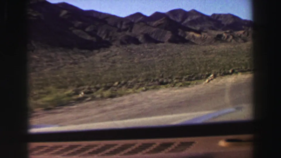 Car-window view of rugged foothills, sparse roadside plants, paved roadway, and open sky in the Lake Tahoe region home movie.