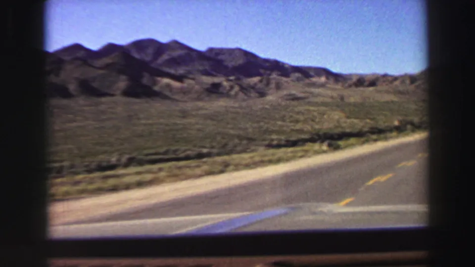 Forward windshield view of a curving road through arid Lake Tahoe-region terrain, with low vegetation and mountain slopes under a clear sky.