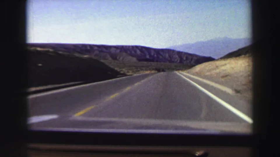 Forward view from a car on a straight two-lane road in the Lake Tahoe area, with dark hills, pale roadside slopes, and distant mountains visible ahead.