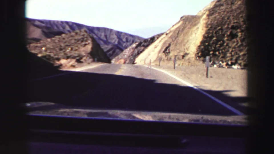 Forward-facing 8mm car view on a curving Lake Tahoe-area mountain road, with dry slopes, roadside posts, and distant ridges.